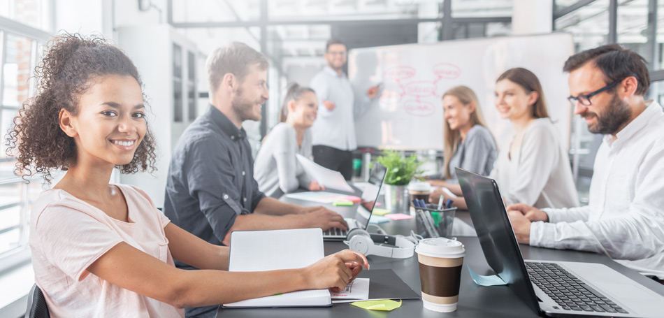 Eine Gruppe von Menschen sitzt an einem Konferenztisch, arbeitet an Laptops und diskutiert. Im Hintergrund ist eine Präsentation zu sehen.